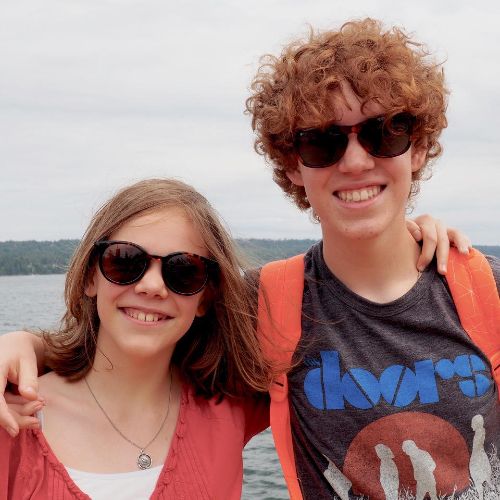 two youth smiling with sunglasses on by the water